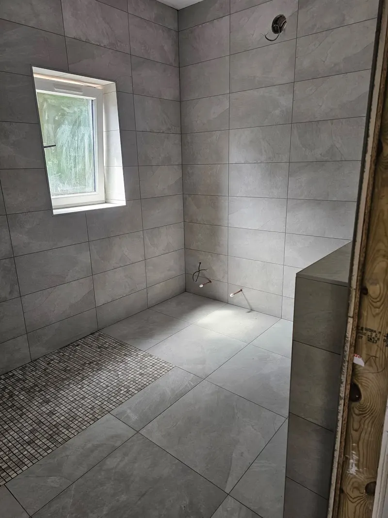 Grey tiled wet room with a mosaic drainage channel