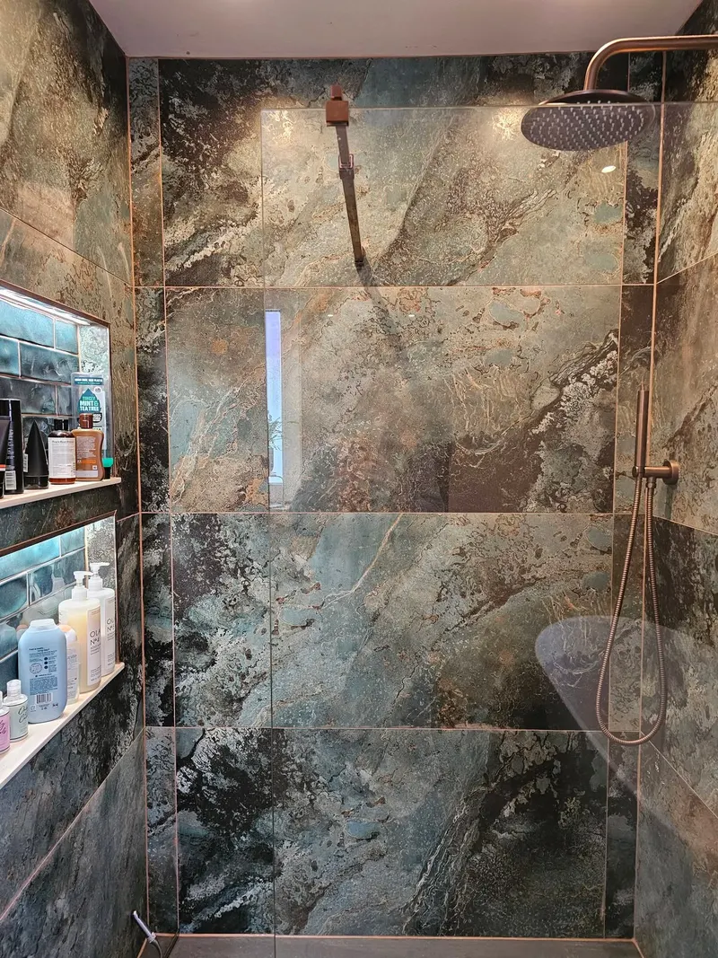 Shower wall tiled in large green and black marble-effect porcelain tiles with a recessed niche