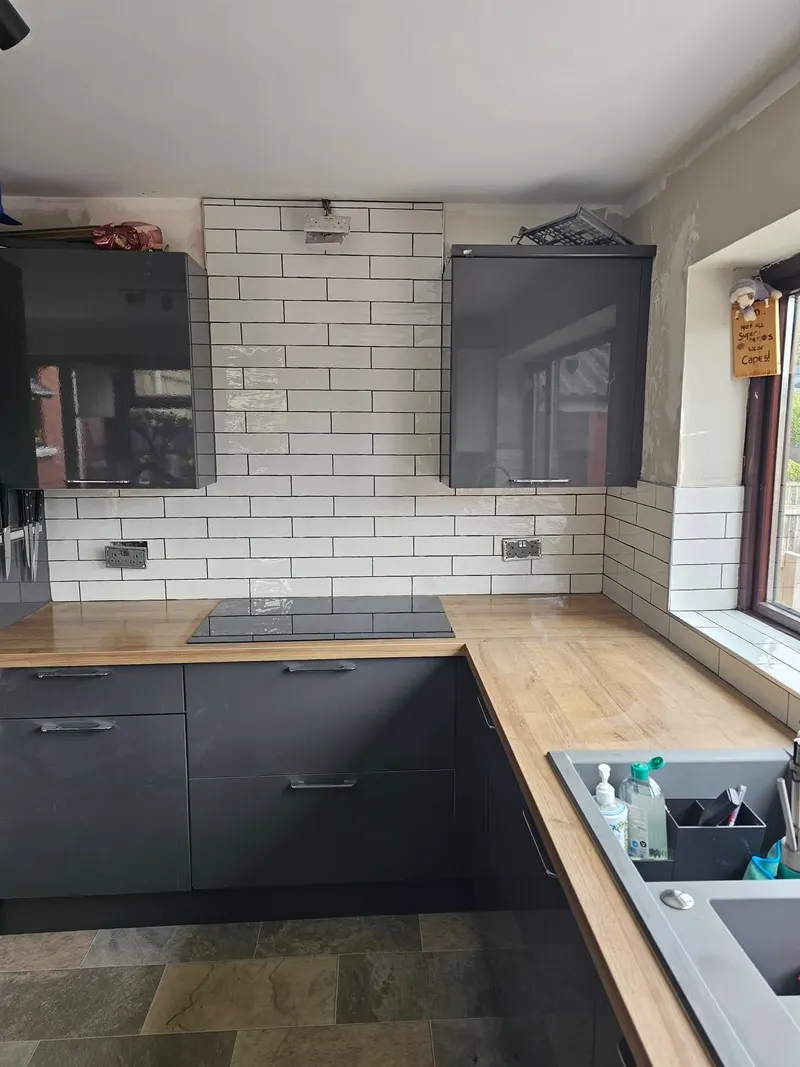 White metro tile kitchen splashback with dark units and a wooden worktop